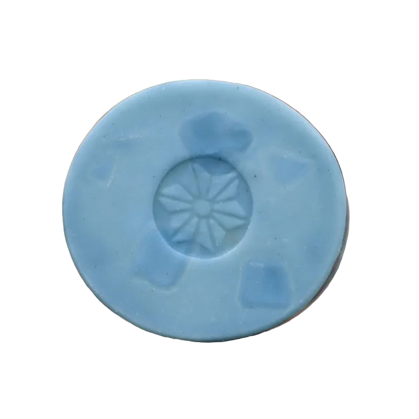 Blue bar soap with a star-like design with blurred red and green foliage in the background