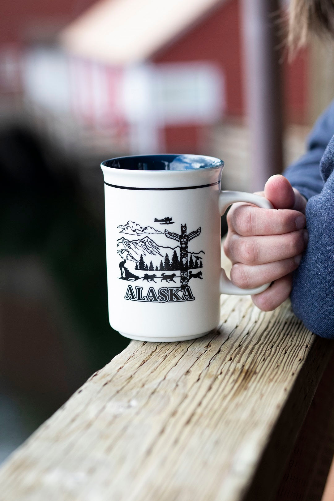 Person holding a mug with an Alaska design on a wooden surface