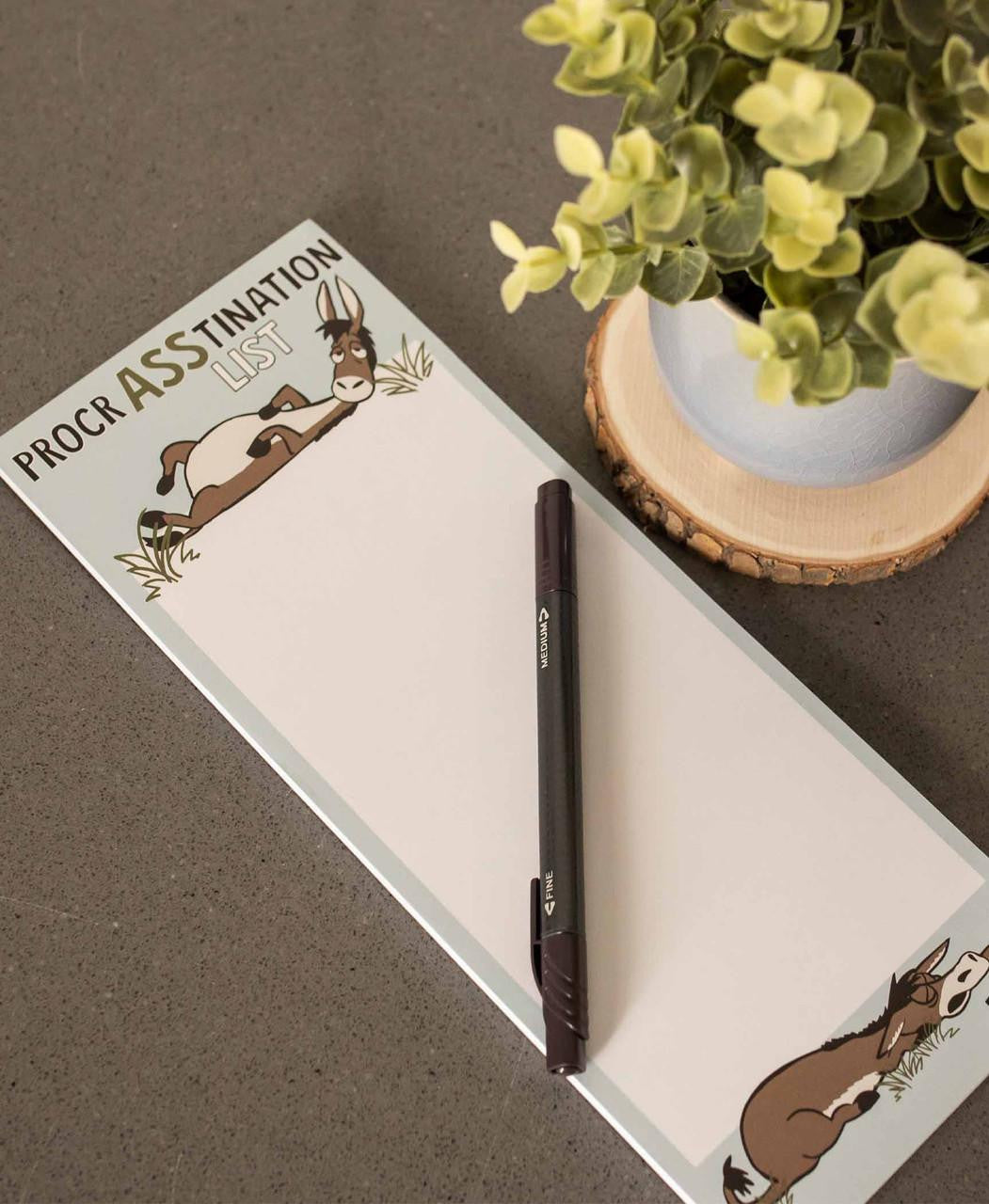 Notepad with donkey illustrations and a pen on a brown surface with a plant in the background