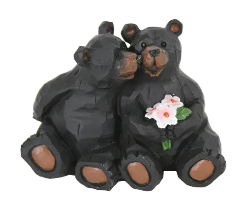Two black bear figurines with a white flower on a white background