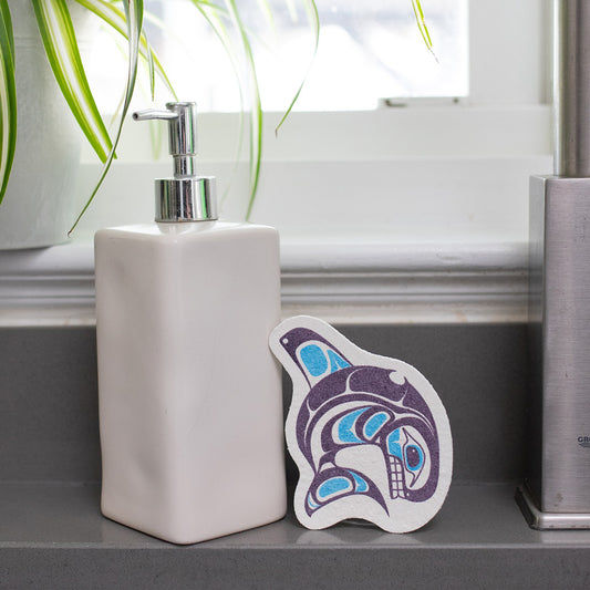 Soap dispenser on a bathroom counter with an eco sponge featuring a purple and blue form line whale design