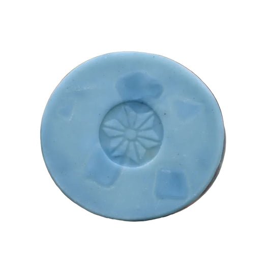 Blue bar soap with a star-like design with blurred red and green foliage in the background