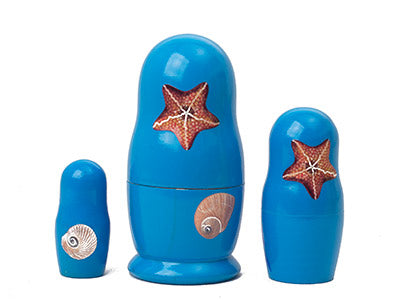 Set of three blue nesting dolls with starfish and shell designs on a white background
