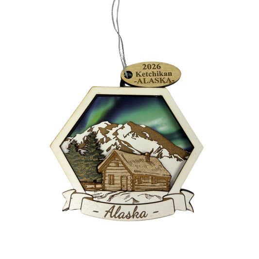 Hexagonal ornament with a log cabin and Northern Lights design, featuring '2026 Ketchikan, Alaska' text.