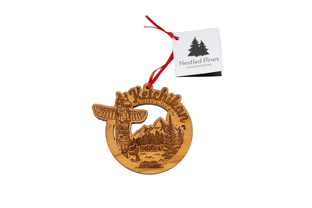 Wooden ornament with 'ketchikan' text and mountain design, hanging from a red string 