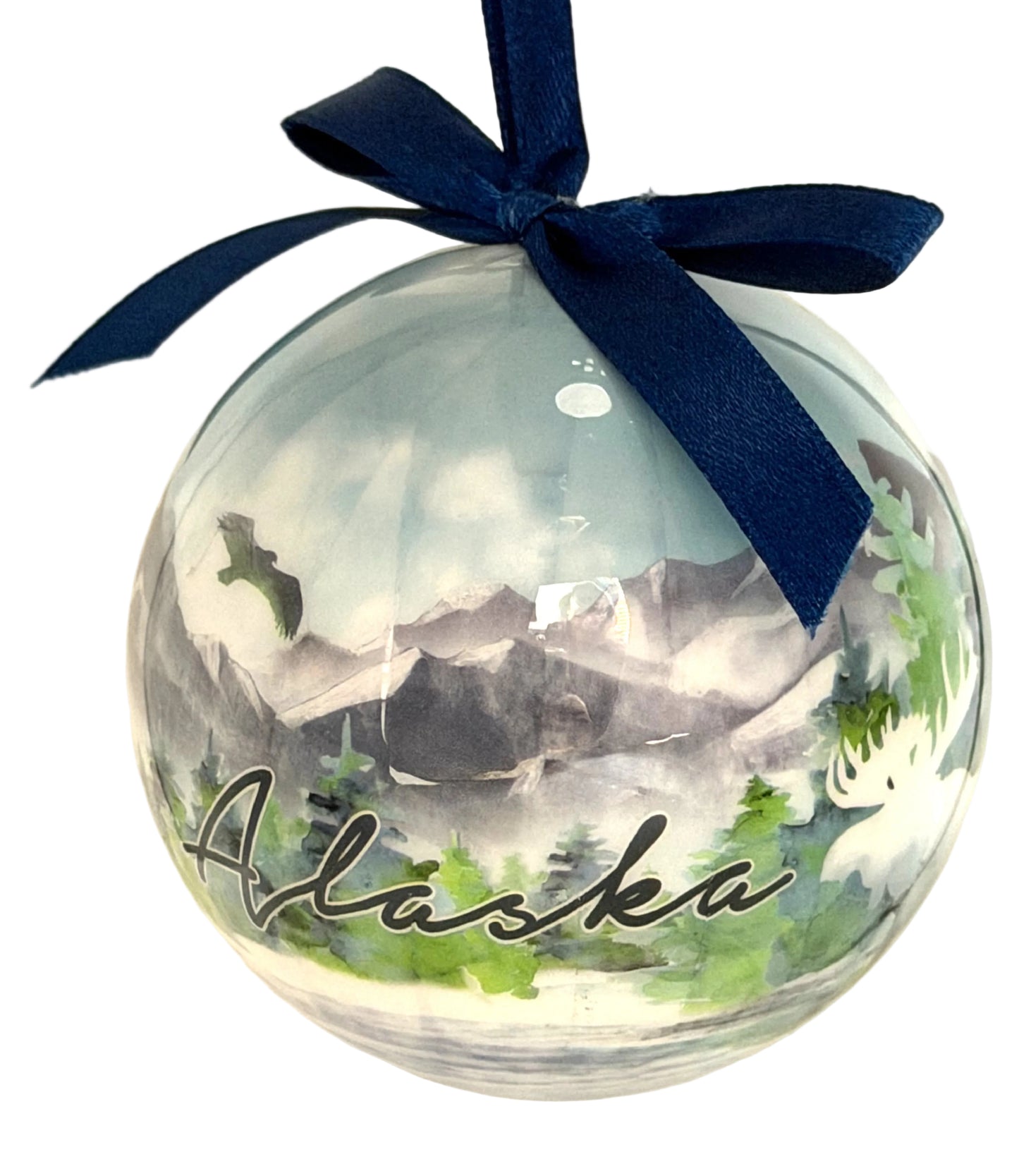 Round ornament with 'Alaska' text, mountain and forest scene, and navy blue ribbon on white background