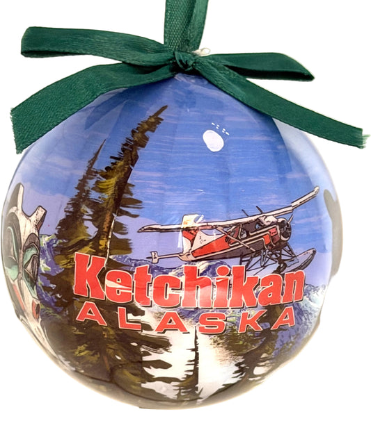 Round ornament with 'Ketchikan Alaska' text and airplane graphic, tied with a green ribbon.