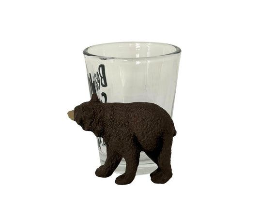 Clear shot glass with a bear-shaped object outside on a white background