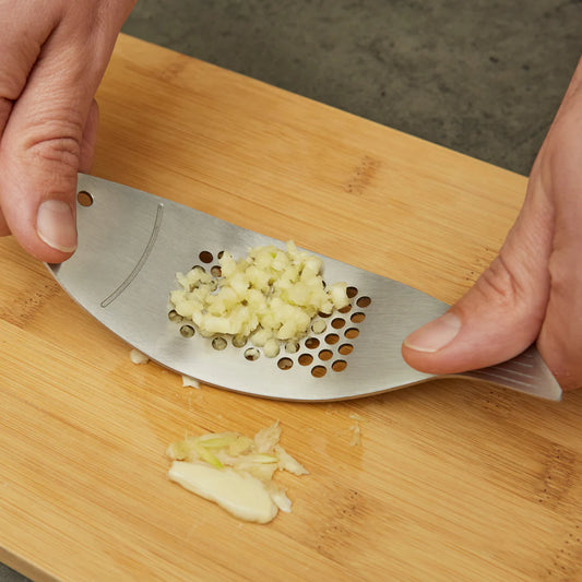 Metal garlic press with minced garlic on a wooden cutting board