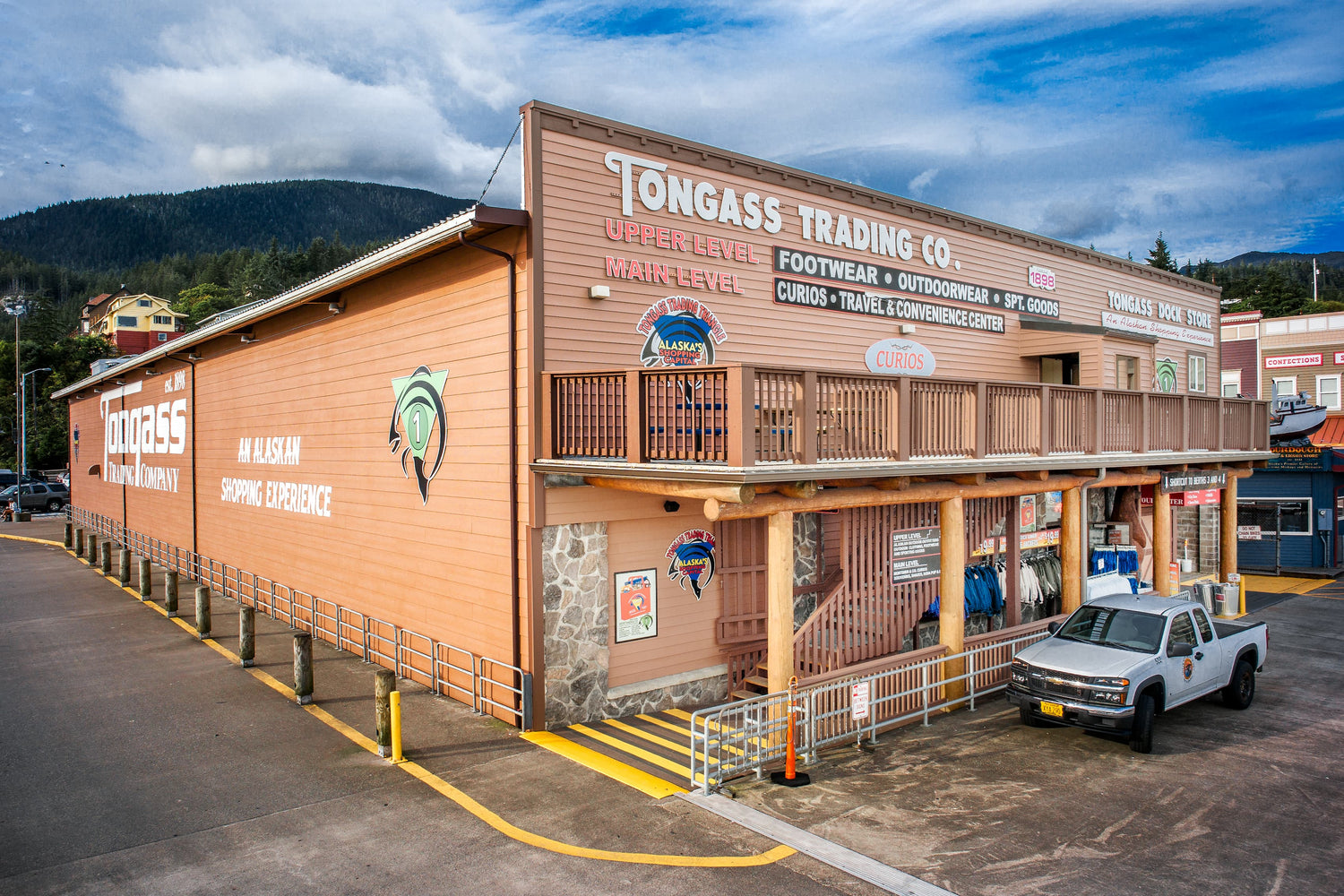 Tongass Trading Co building with a white truck parked in front, surrounded by mountains and trees.