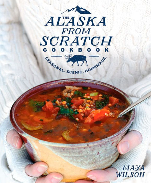 Bowl of soup held by a person with 'The Alaska From Scratch Cookbook' in the background