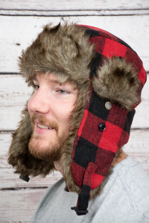 Person wearing a red and black plaid hat with fur trim against a wooden background