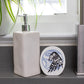 White soap dispenser with an Eco-sponge with formline art of a raven and a moon, on a bathroom shelf.